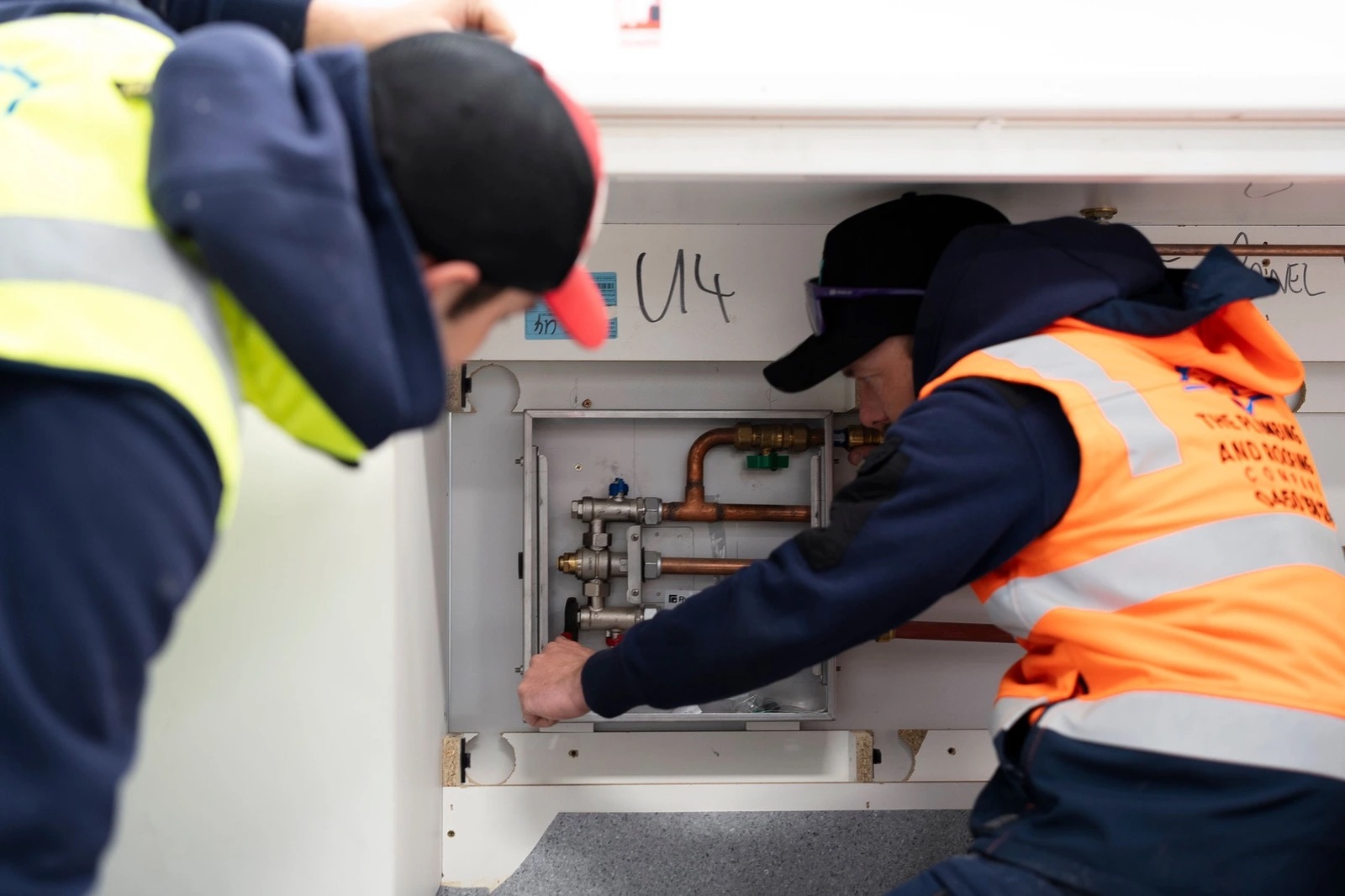 Two plumbers inspecting a thermostatic mixing valve in a service cabinet